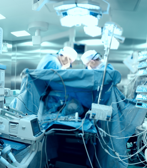 In advanced operating room with lots of equipment, patient and working surgical specialists